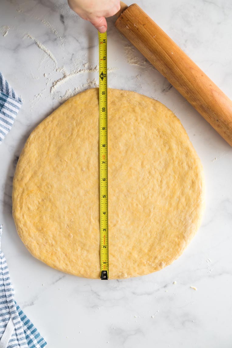 a circle of donut dough with a measuring tape showing 11 inches wide 