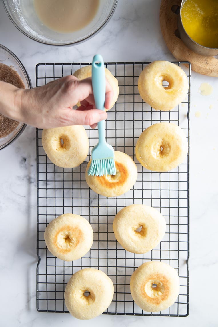 donuts on a cooling rack being brushed with butter