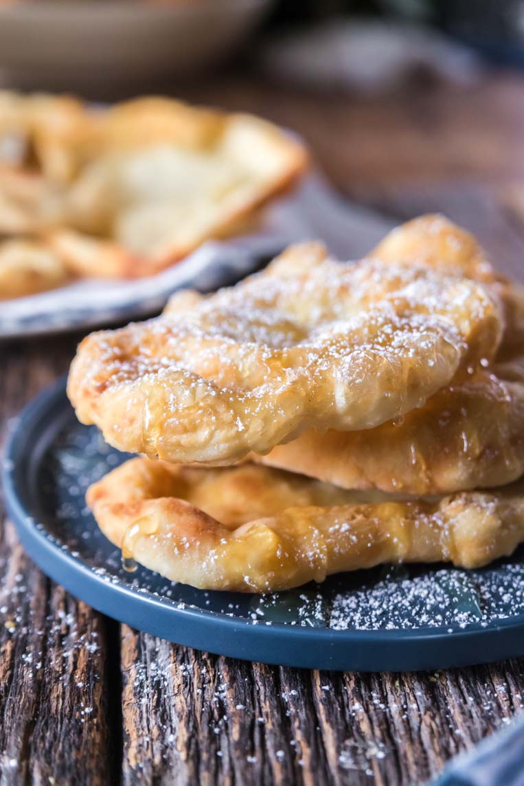 a stack of Indian fry bread on a plate with honey and powdered sugar