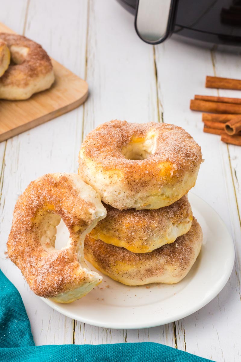 a stack of air fryer cinnamon biscuit donuts on a plate; one with a bite out of it