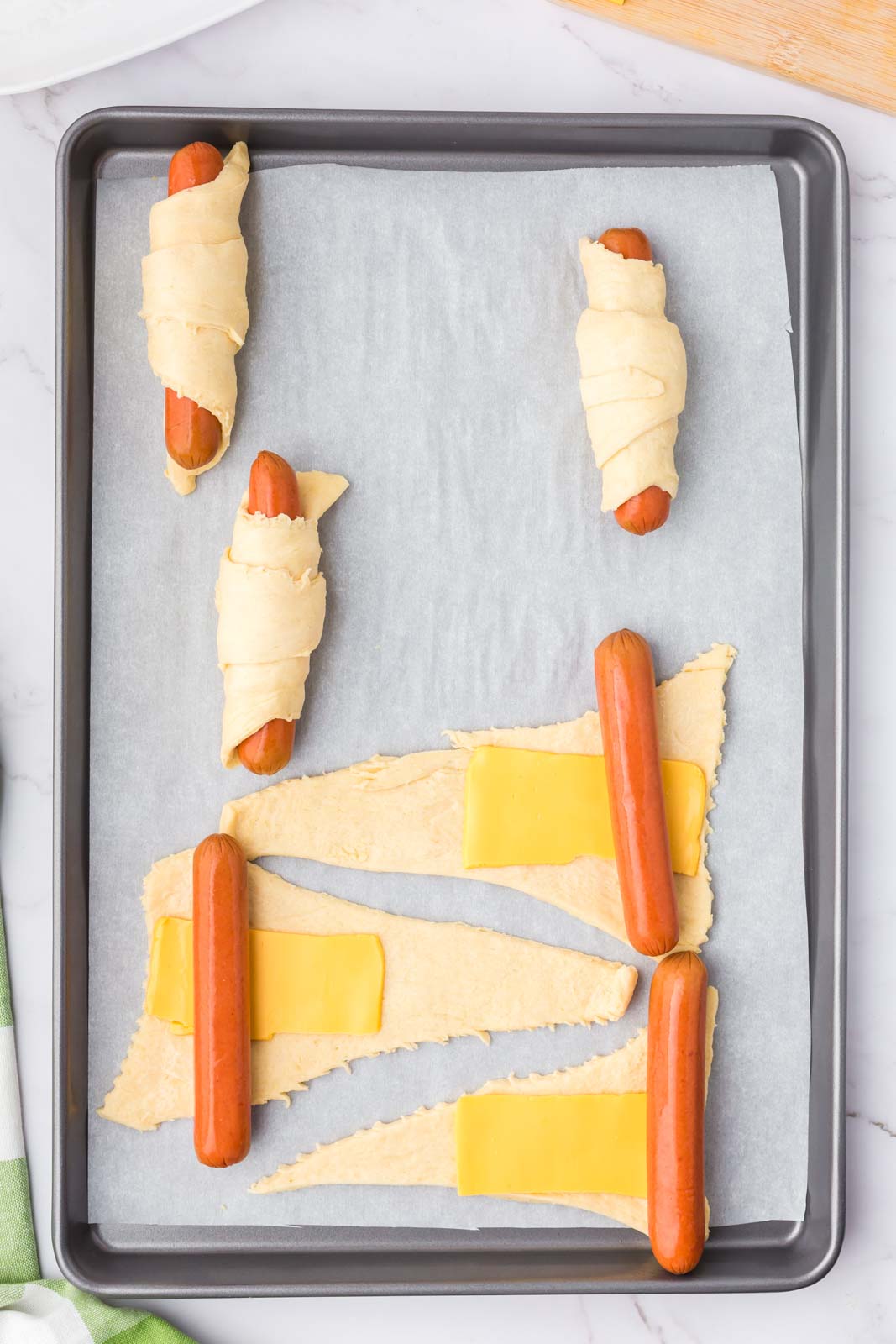 a cookie sheet with partially rolled hot dogs and some being rolled in dough 