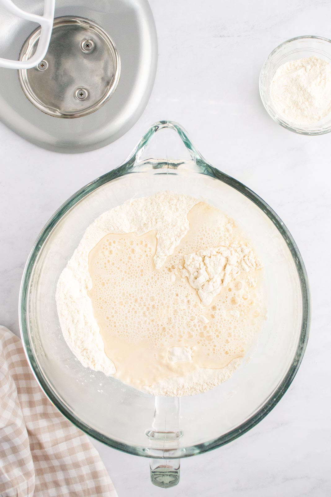 a glass mixing bowl with flour, yeast, water and salt