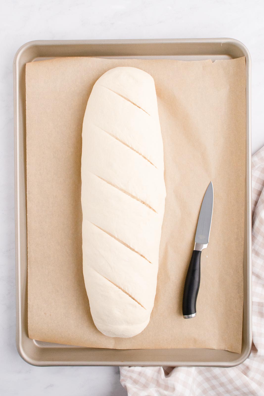 a rested french bread loaf with slashes cut in the top before baking
