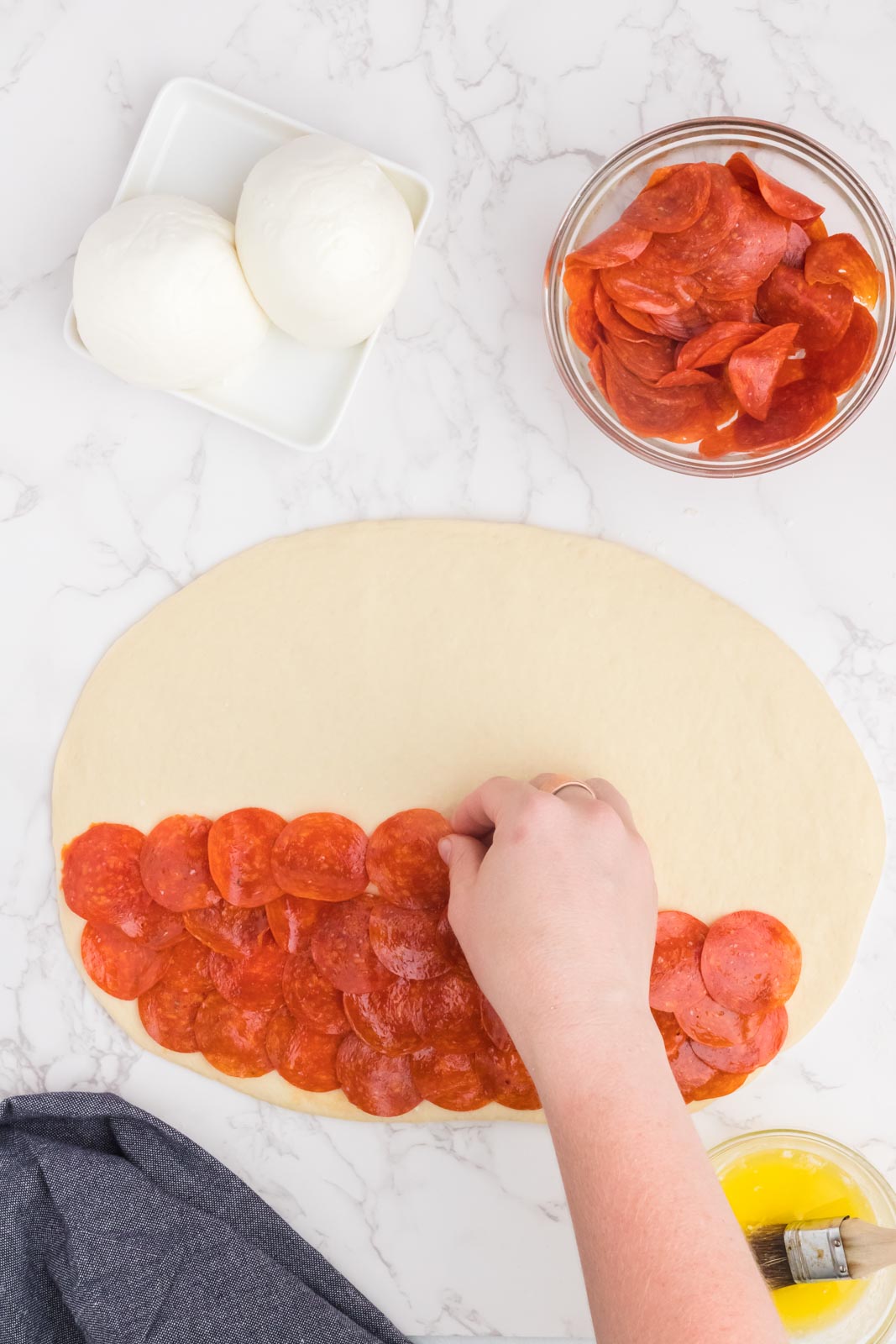 rolled out pizza dough with a hand layering on small pepperoni 