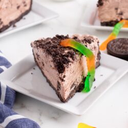 Slices of Oreo dirt pie served on plates and topped with gummy worms.