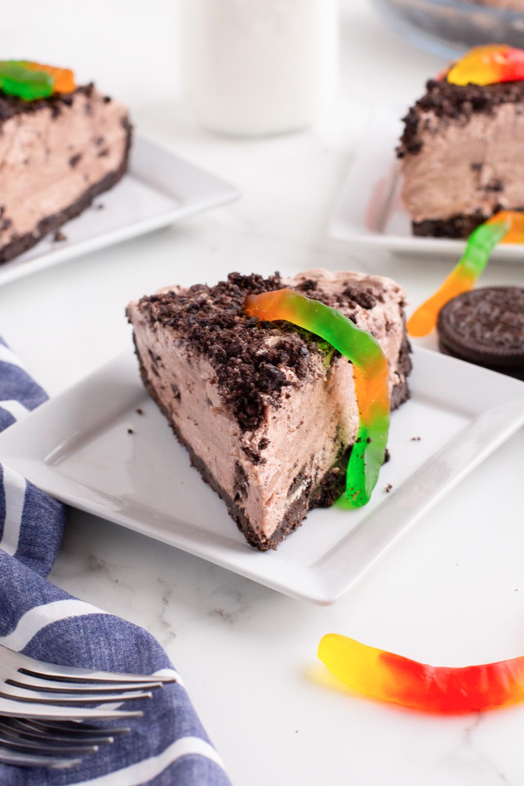 Slices of Oreo dirt pie served on plates and topped with gummy worms.